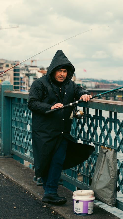 Man in Long Coat Raincoat Holds Fishing Rod on Galata Bridge in Istanbul