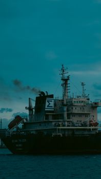 Majestic cargo ship emits smoke while sailing through calm waters at twilight, showcasing maritime industry.