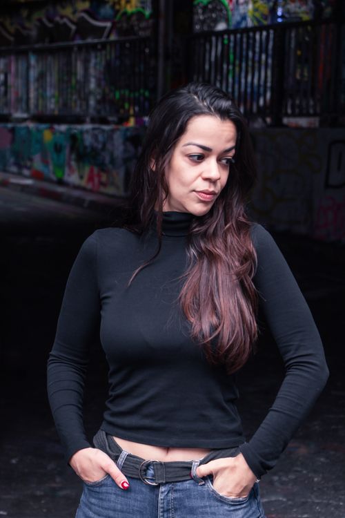 Free Woman in black turtleneck with hands in pockets standing in urban graffiti setting. Stock Photo