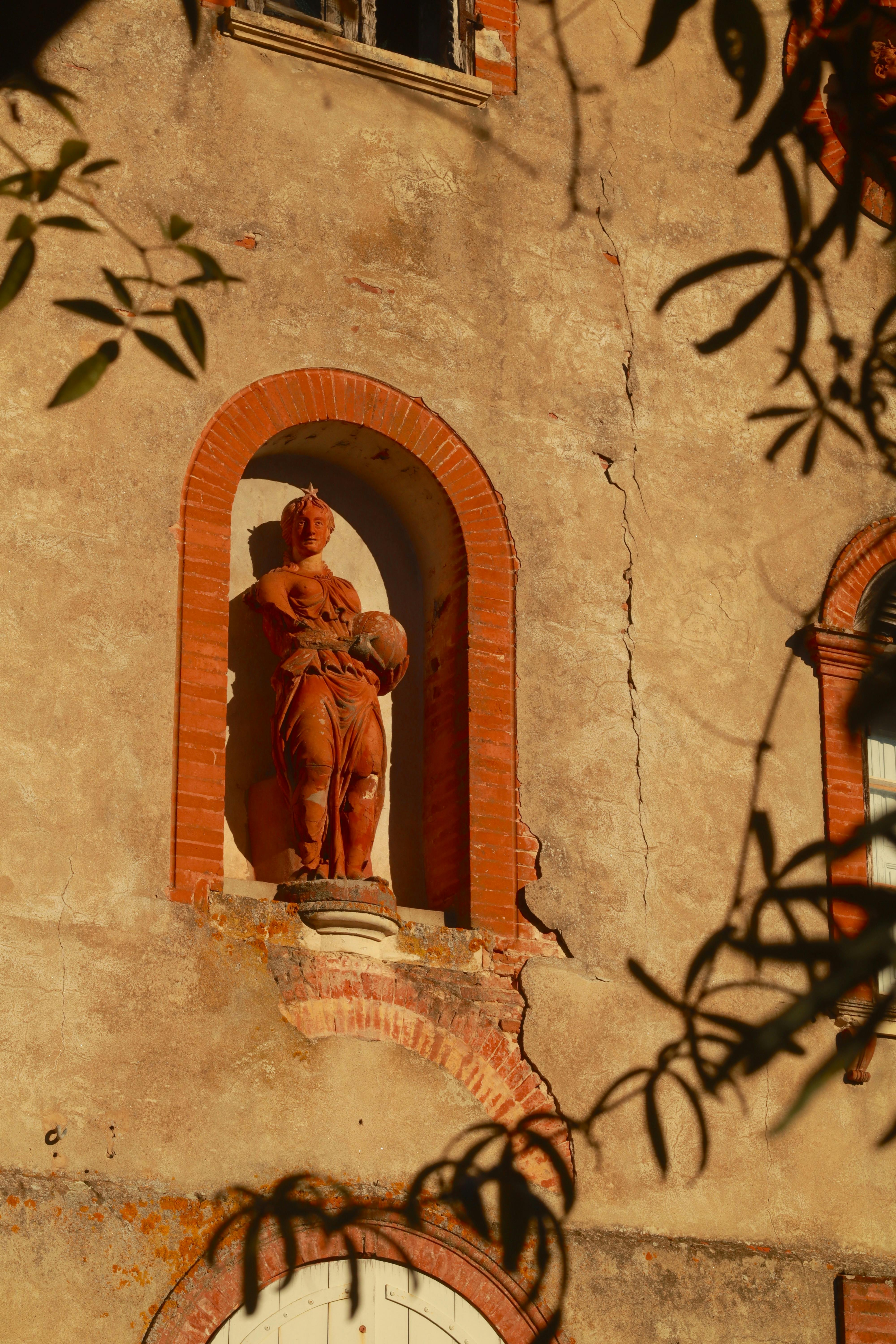 Sunlit historic facade with a vintage sculpture in an arched niche, surrounded by shadows.