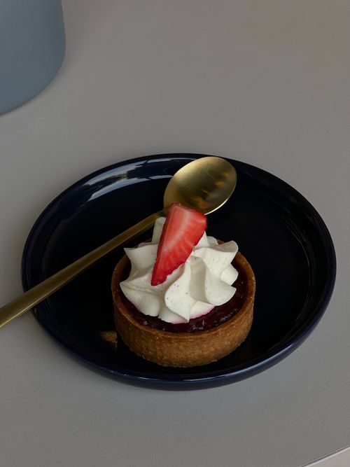 Free Elegant strawberry tart topped with cream, served on a stylish blue plate with a gold spoon. Stock Photo