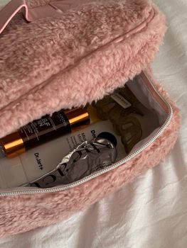 A close-up of a pink furry bag containing skincare and cosmetic products.