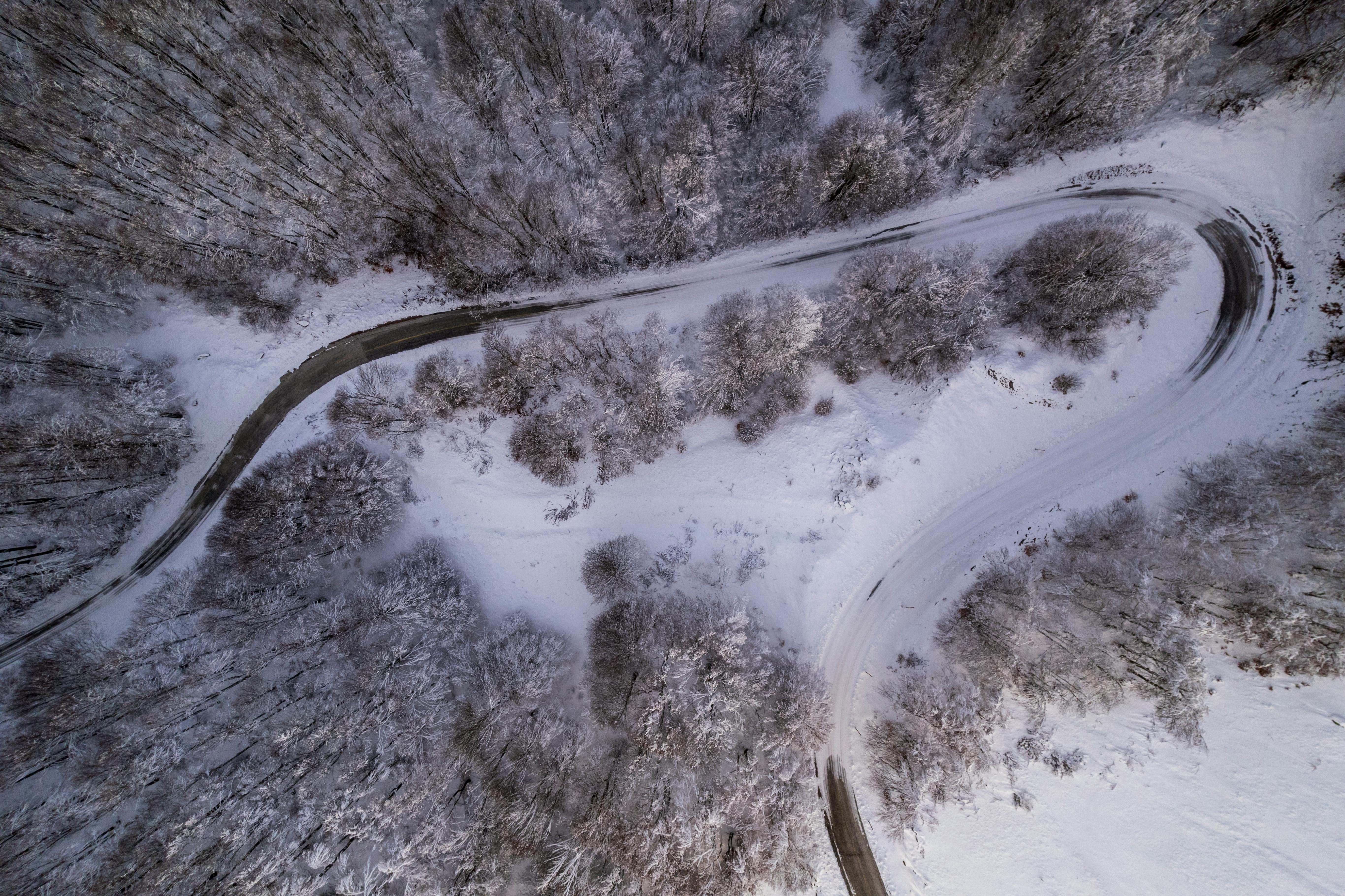 Drone view of a snow-covered forest and winding road in Καστοριά, Greece, showcasing a serene winter landscape.