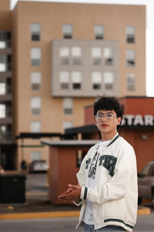 Free Casually dressed young man in glasses posing confidently on a city street with buildings in the background. Stock Photo