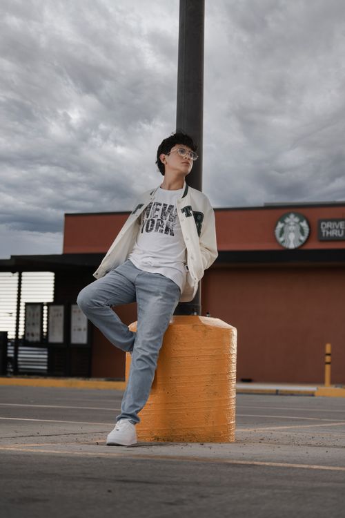 Free Stylish man in casual outfit poses by a pole on an urban street with cloudy sky. Stock Photo
