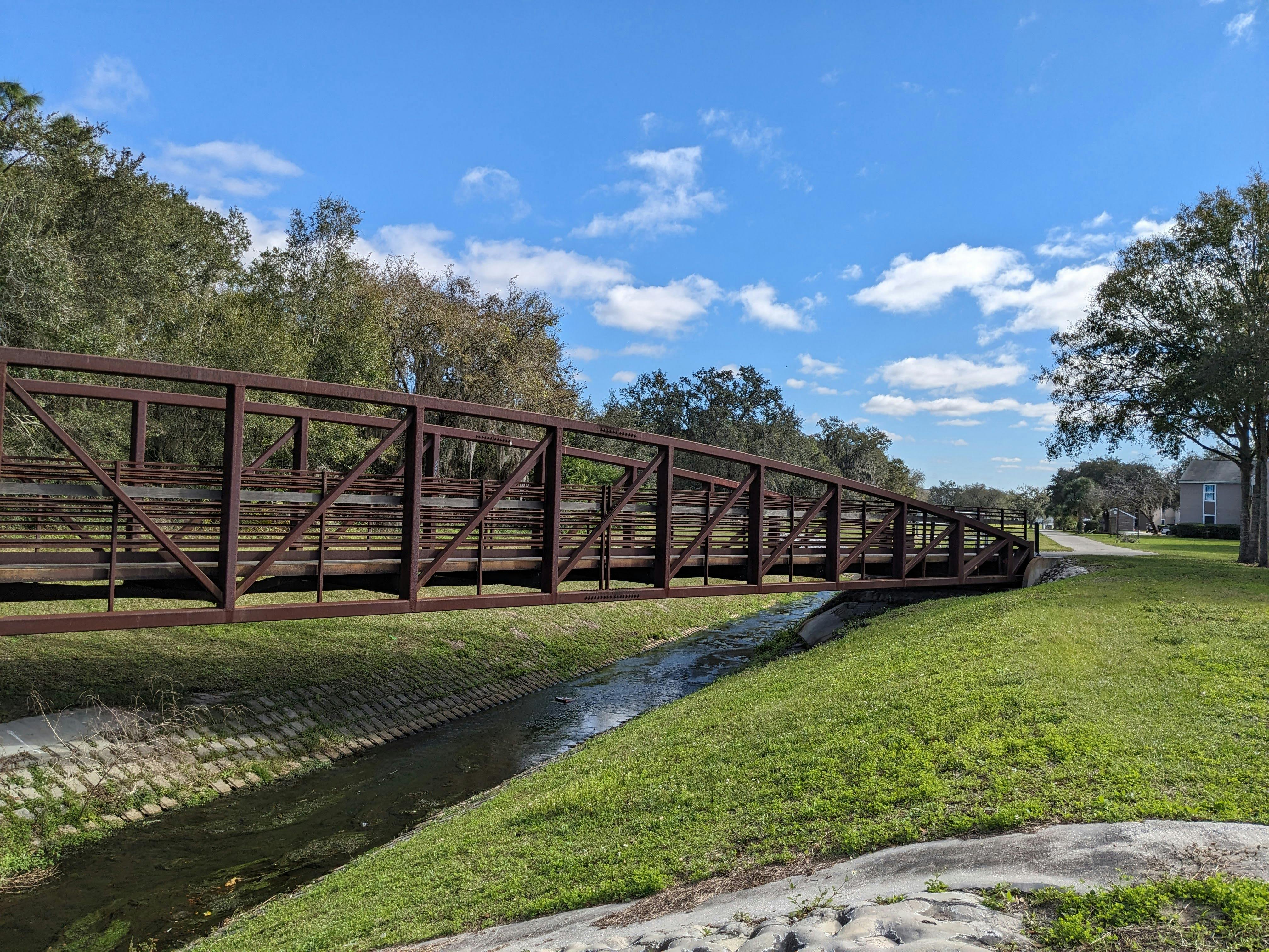 A rustic footbridge spans a quiet stream under a clear blue sky in Kissimmee, Florida.