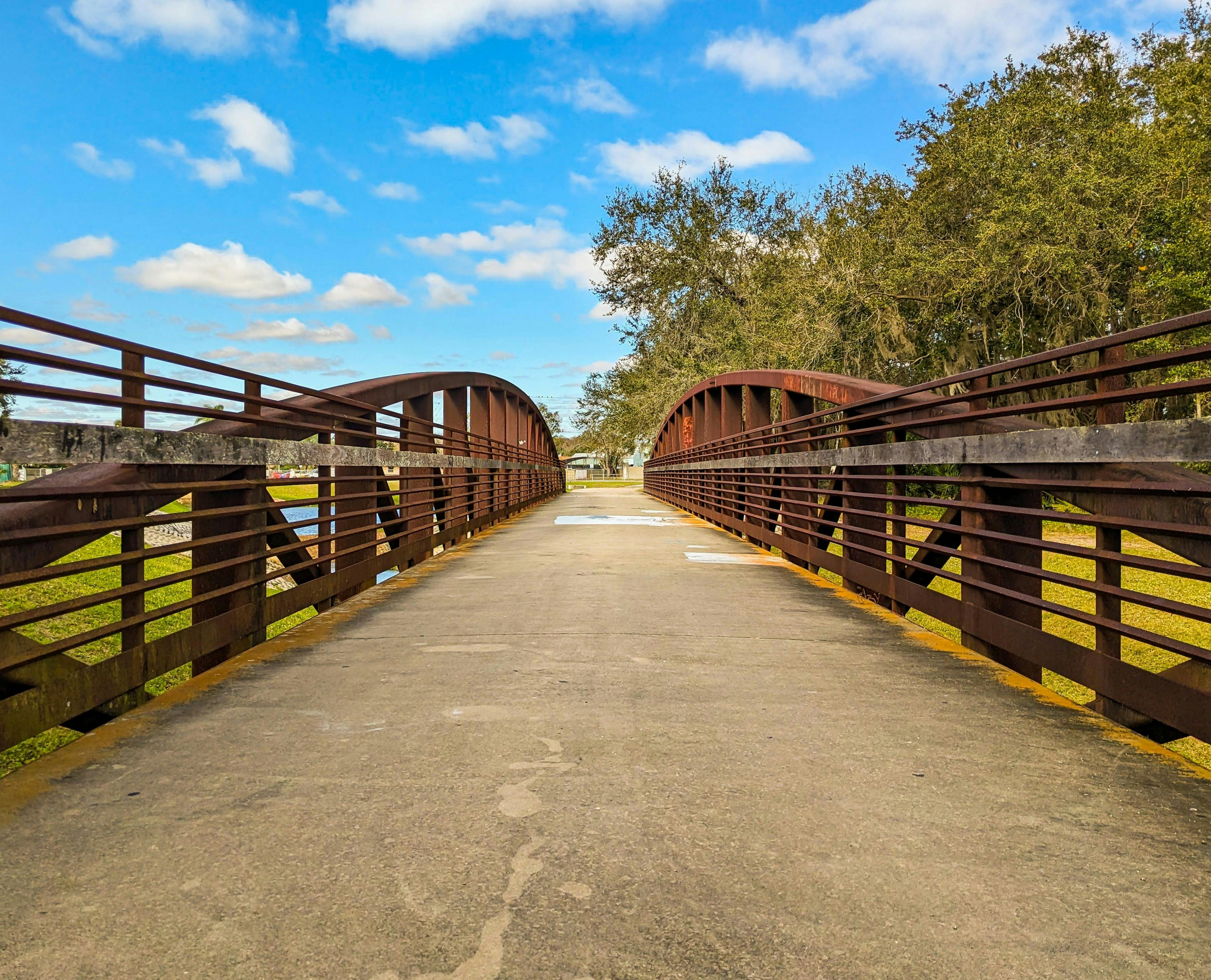 Wooden bridge in Kissimmee Park under a bright blue sky with clouds and trees.