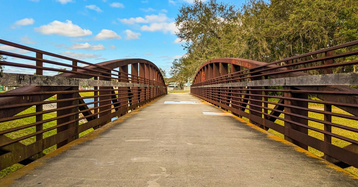 Wooden bridge in Kissimmee Park under a bright blue sky with clouds and trees.
