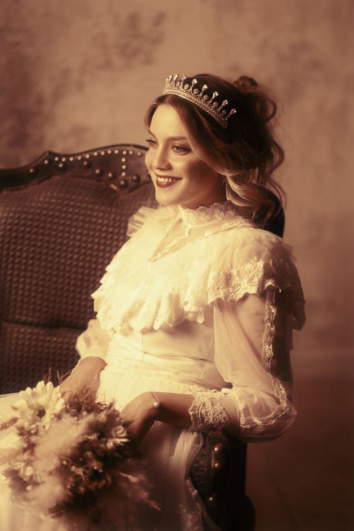Free Portrait of an elegant woman in a Victorian-style gown with a tiara, sitting gracefully indoors. Stock Photo