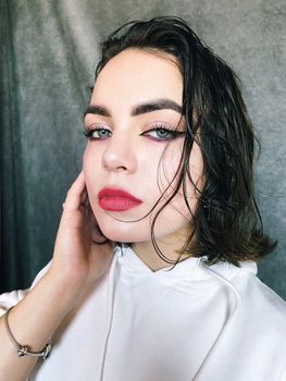 Close-up portrait of a woman with bold makeup and wet hair, wearing a white hoodie.