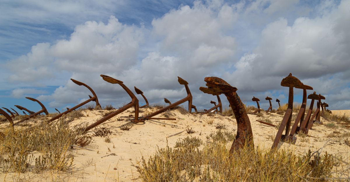Scenic view of rusted anchors protruding from sand on a sunny beach day.