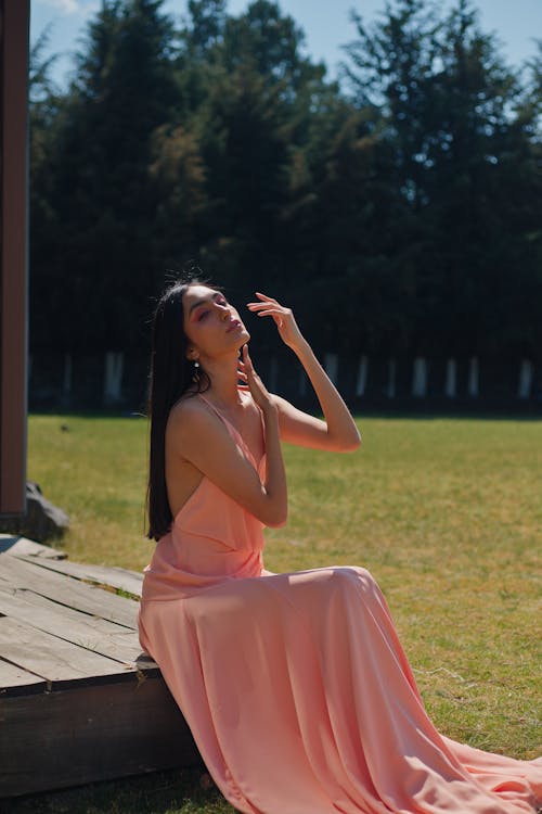 A woman in a pink dress sitting on a wooden deck