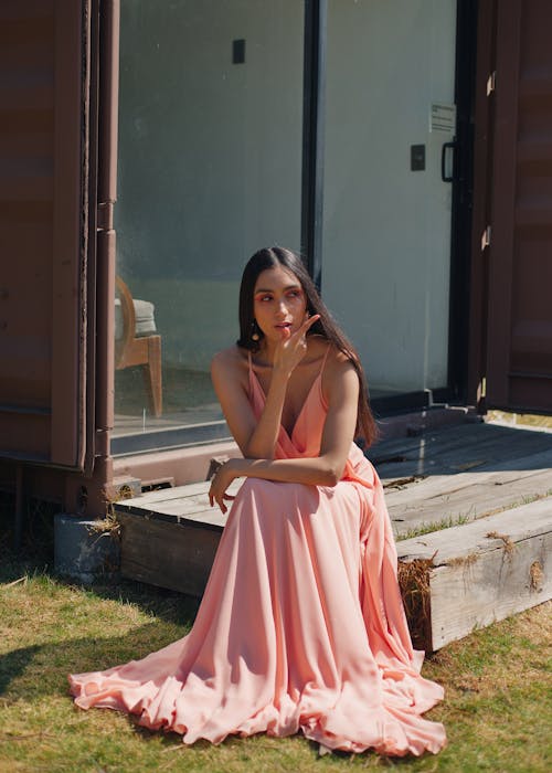 A woman in a pink dress sitting on the grass