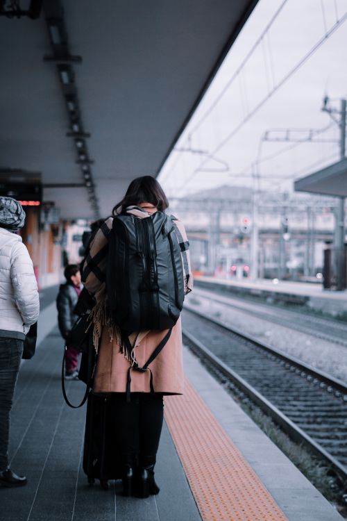 Free A person with a backpack stands at a railway station platform, waiting for the train to arrive. Stock Photo