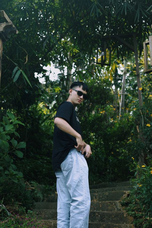 Free Man in black t-shirt and white pants poses confidently in a green forest landscape. Stock Photo