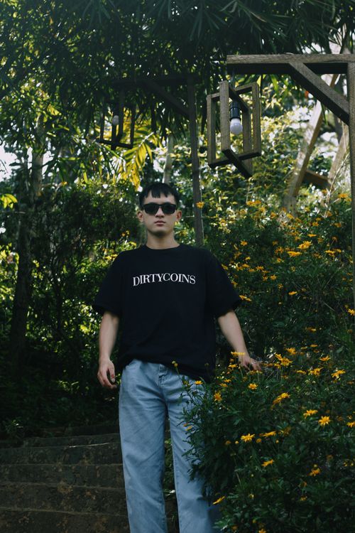 Free Stylish man in sunglasses and black t-shirt standing amidst vibrant flora in a forest. Stock Photo