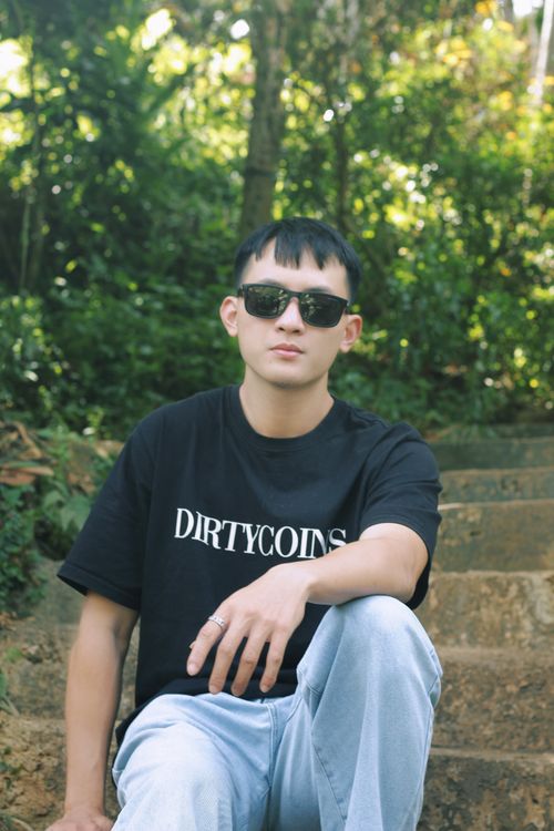 Free Casual young man in sunglasses and t-shirt relaxing on outdoor stone steps surrounded by greenery. Stock Photo
