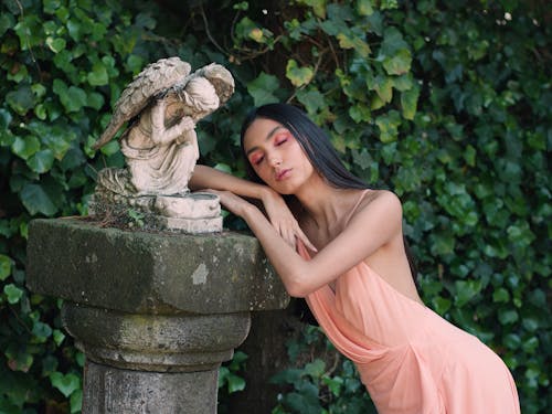 A woman in a pink dress leaning against a stone statue