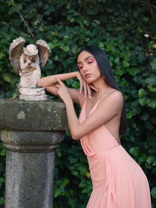 A woman in a pink dress posing next to a statue