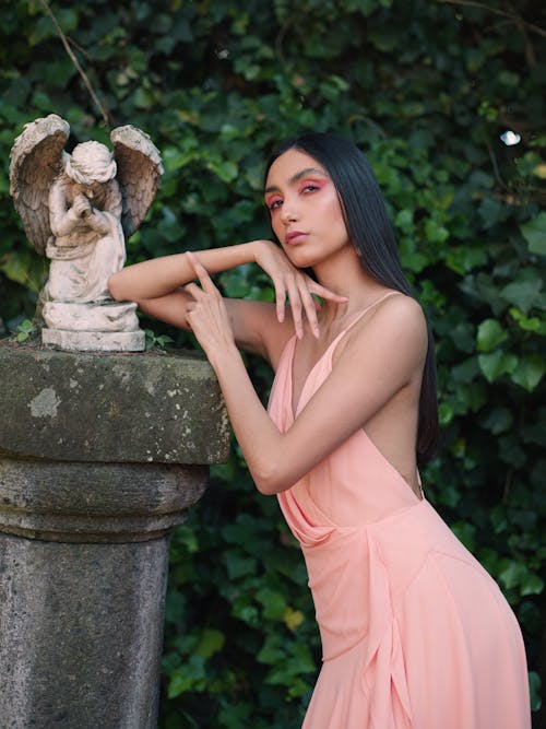 Young Woman in a Pink Dress Posing by the Statue of an Angel 