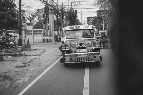 Free A classic jeepney navigating through urban traffic on a city street, captured in monochrome. Stock Photo
