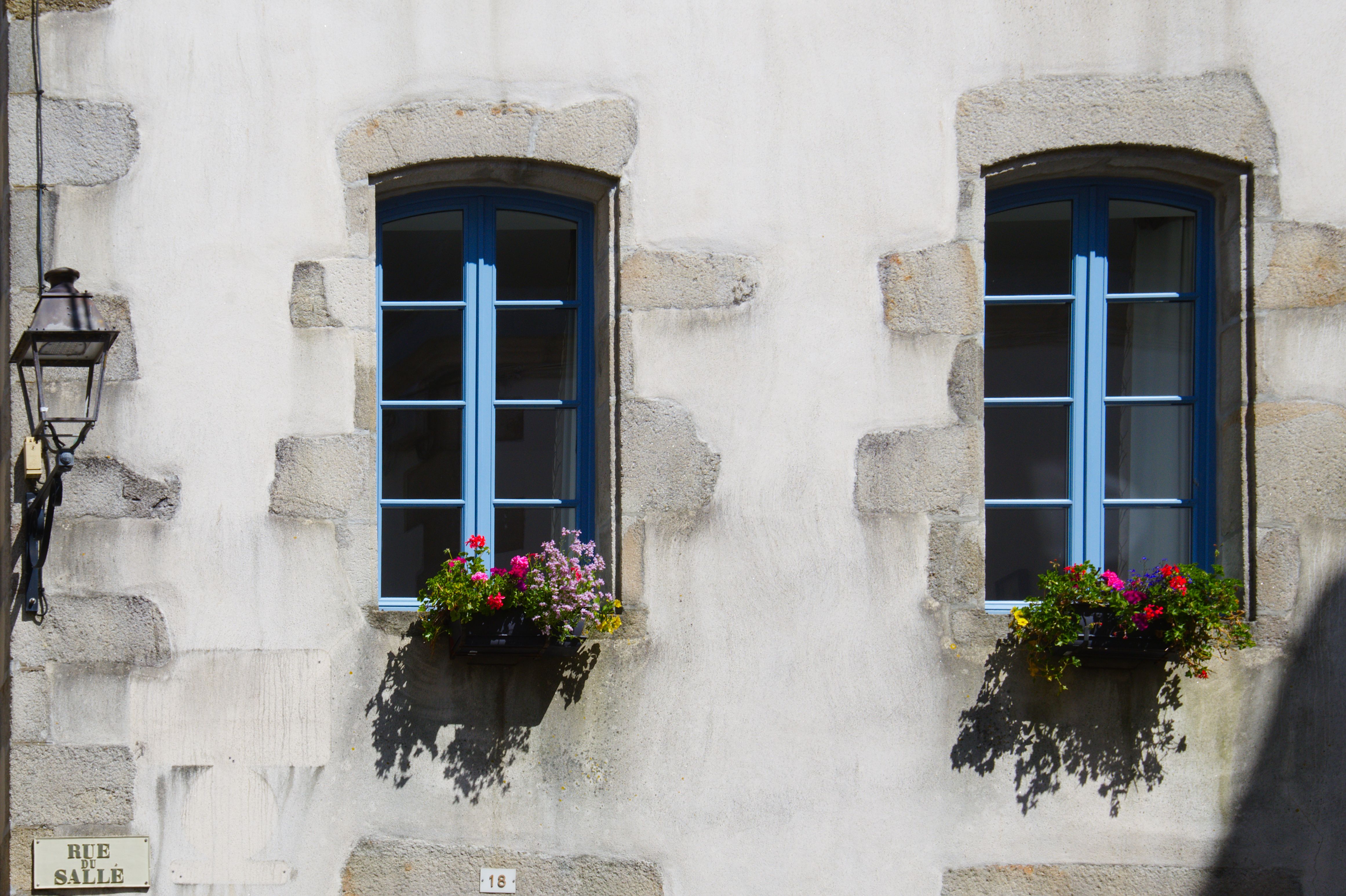 Quaint windows with flower pots on Rue Salle in Quimper, France, showcasing classic French architecture.