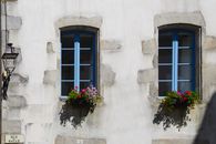 Quaint windows with flower pots on Rue Salle in Quimper, France, showcasing classic French architecture.