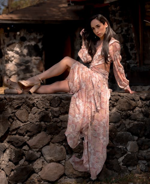 A woman in a floral dress sitting on a rock wall