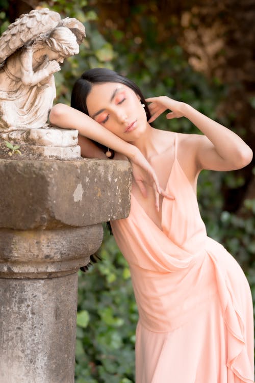 A woman in a pink dress leaning against a stone statue