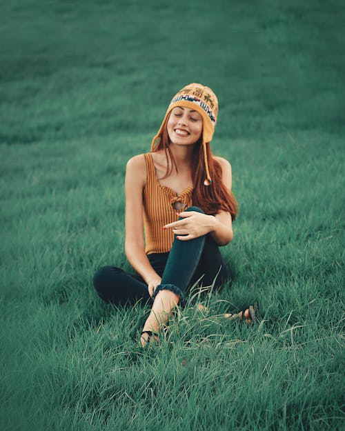 Free Smiling Woman Wearing Brown Sleeveless Shirt Sitting on Grass Field Stock Photo