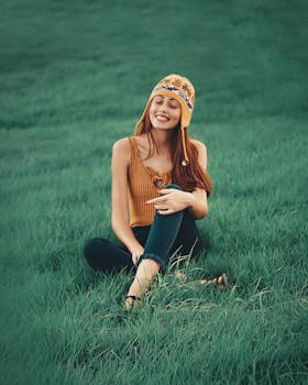 一位快乐的年轻女子身着休闲装，闭着眼睛微笑，坐在绿色的田野上