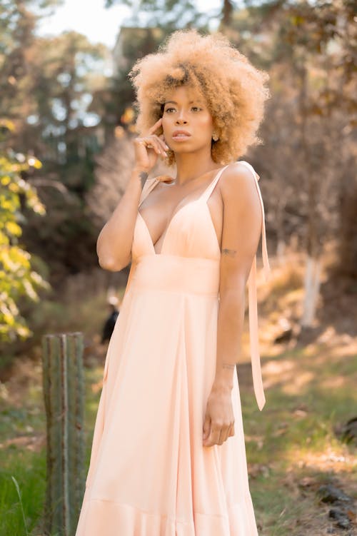 A woman in a peach dress is standing in the woods