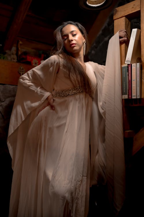 A woman in a long robe posing in front of bookshelves