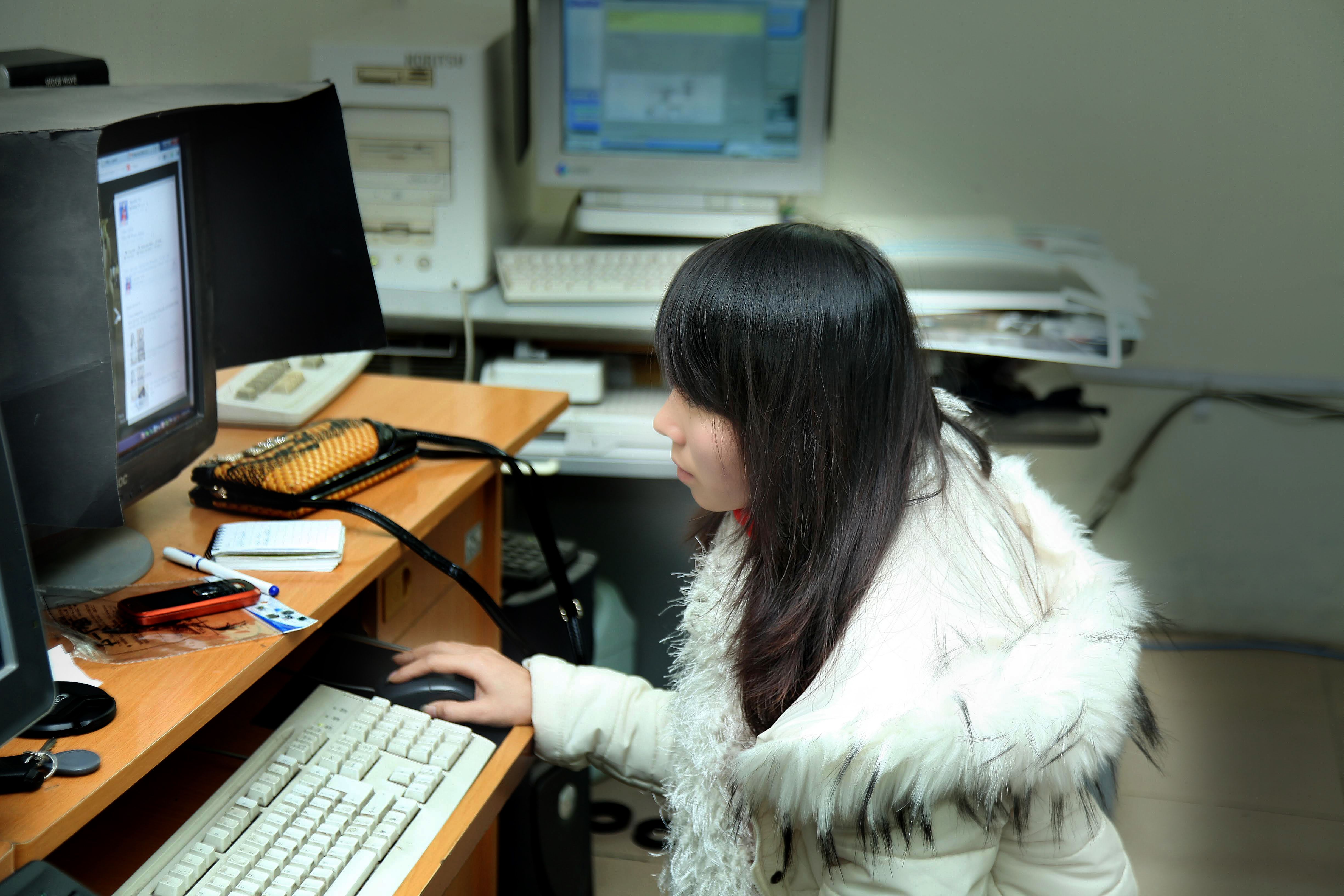 A woman sits at an office desk working on a computer. Cozy winter attire.