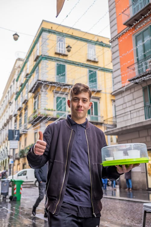 Man in Jacket Holding Box with Cups on Street in Rain