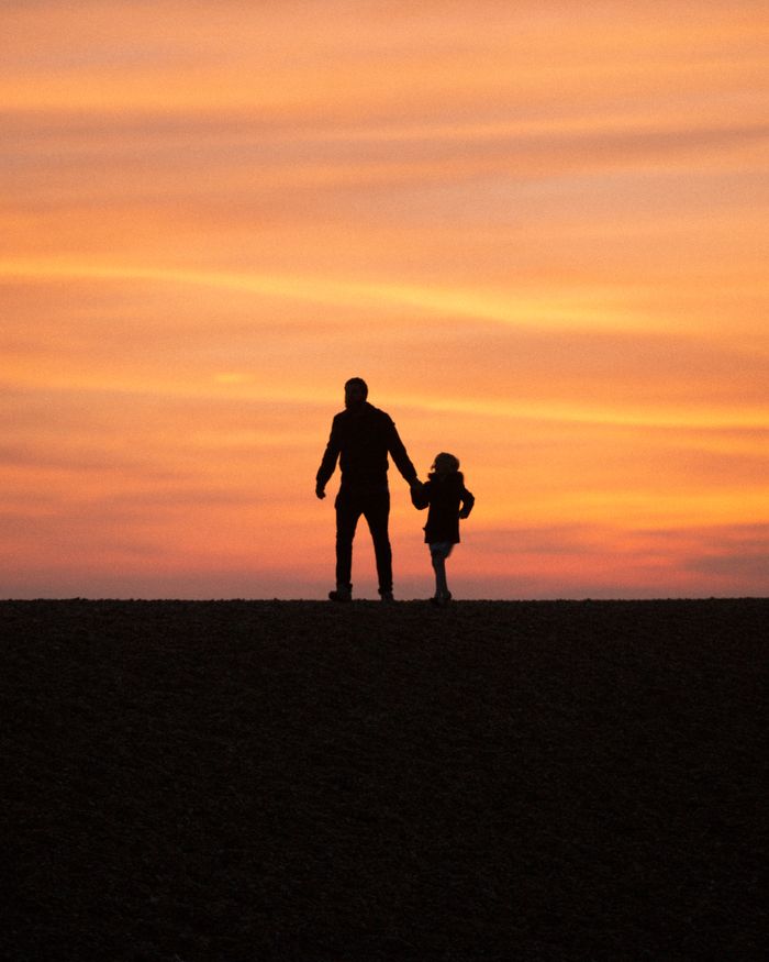 Silhouette of a father and daughter walking hand in hand at sunset