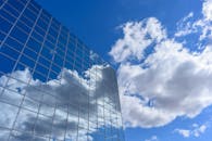 现代城市建筑设计中，玻璃立面的摩天大楼倒映着云朵和蓝天