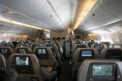 Free In-flight view of an aircraft cabin featuring passengers, flight attendants, and seatback screens. Stock Photo