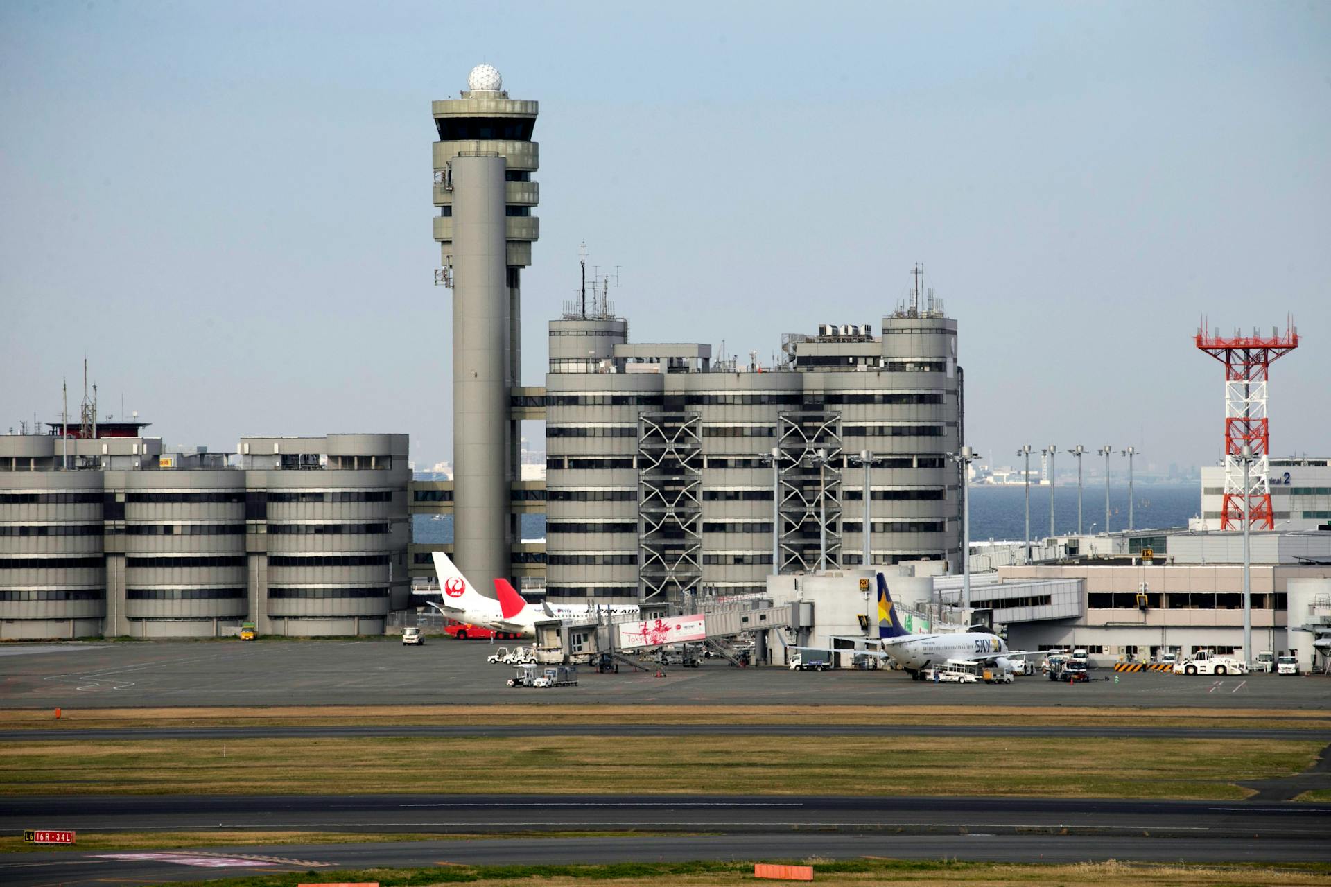 Aerial view of Haneda Airport featuring airplanes, control tower, and terminal buildings in Tokyo, Japan.