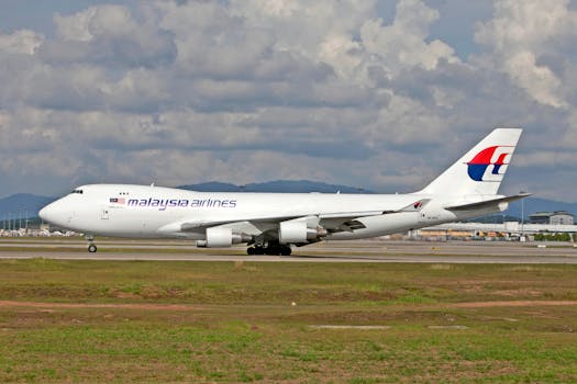 Side view of a Malaysia Airlines cargo jet on the runway with a cloudy sky backdrop.