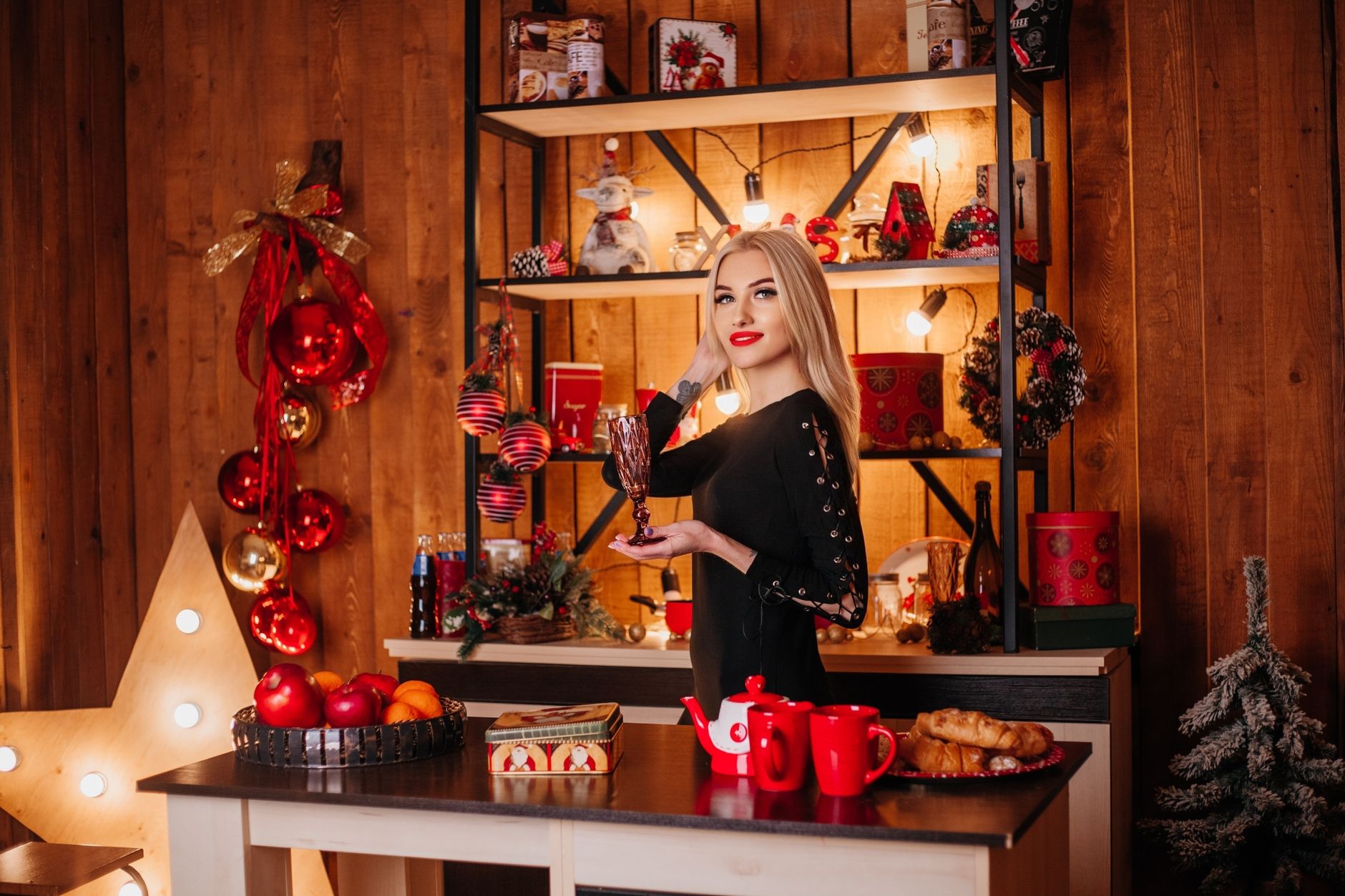Stylish woman with blonde hair holding a glass in a festive Christmas setting.