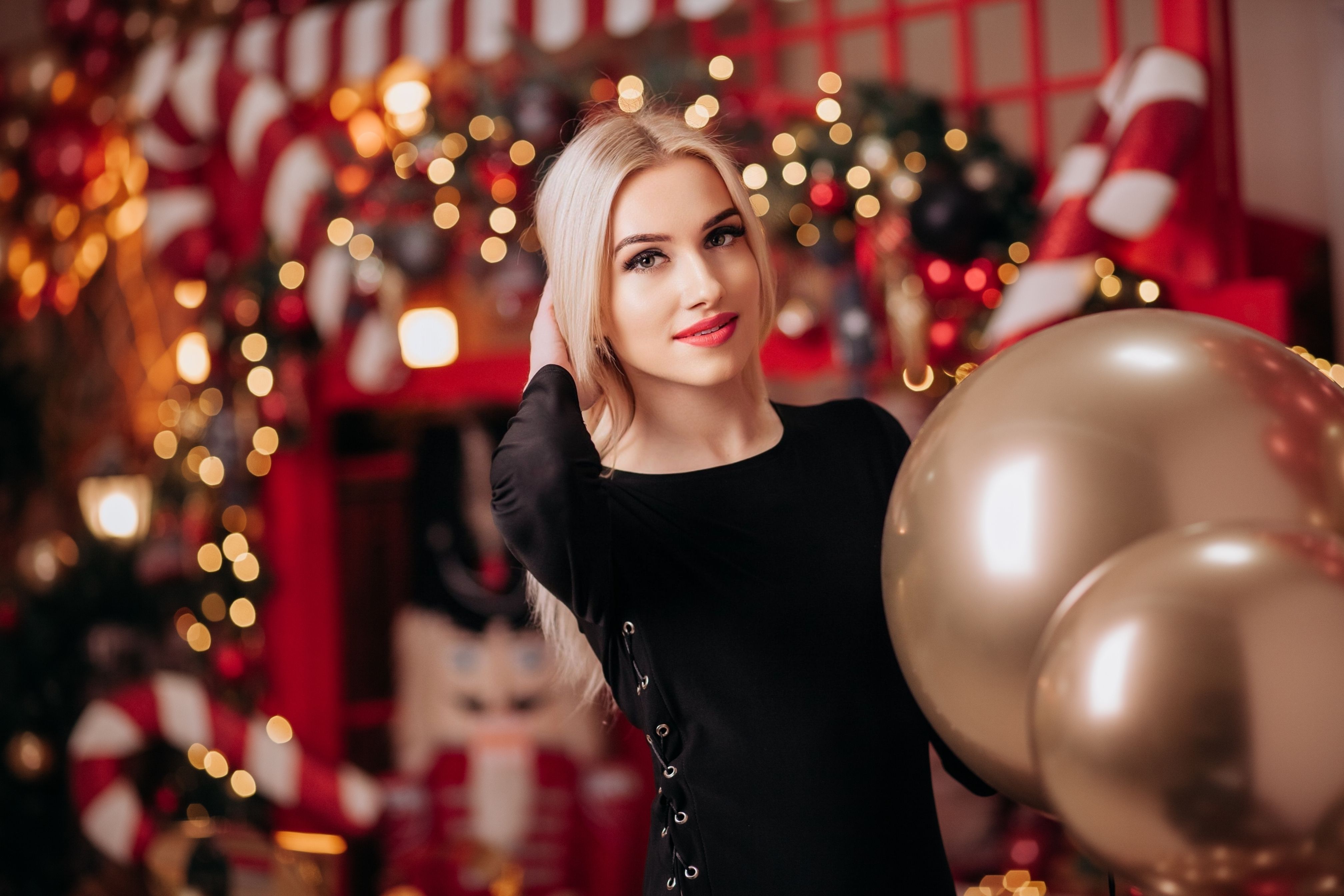 Portrait of a woman in a black dress holding gold balloons amidst Christmas decorations.