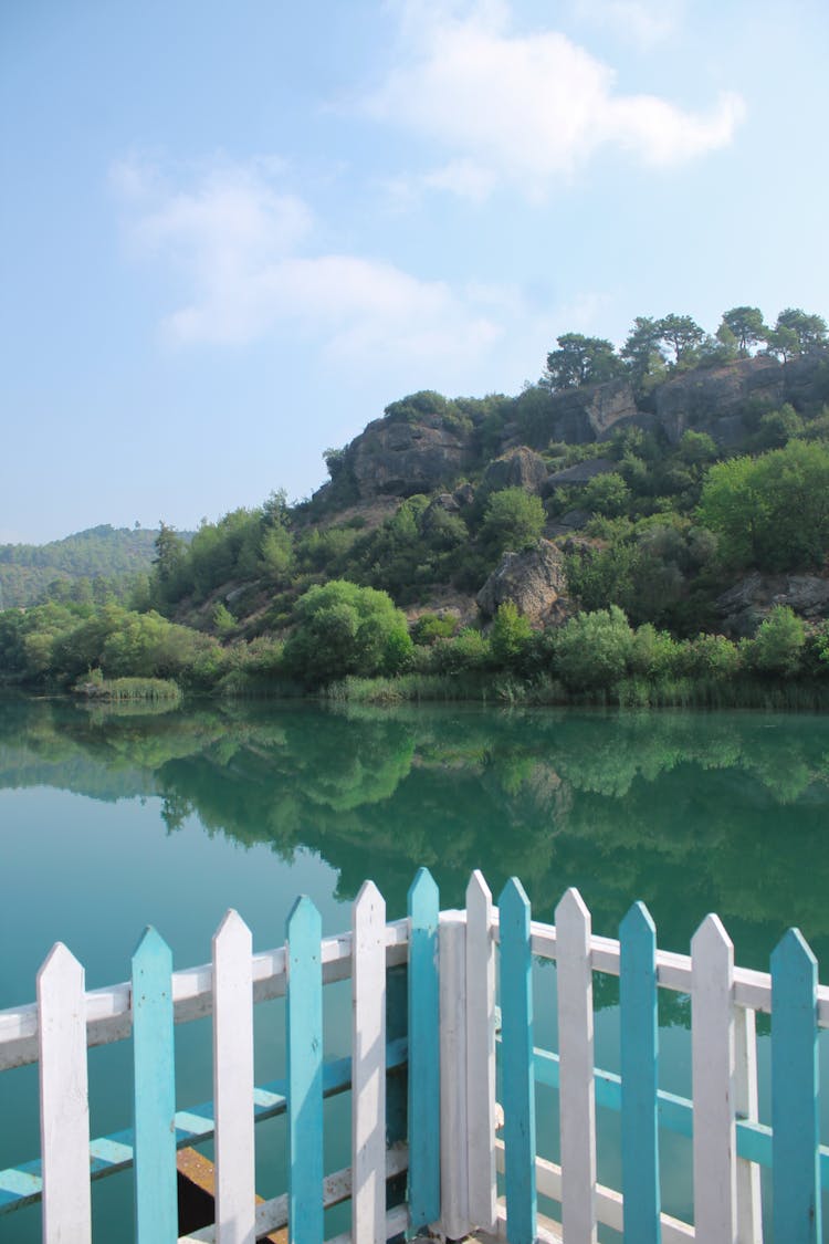 Lake And Hill With Trees Behind Fence