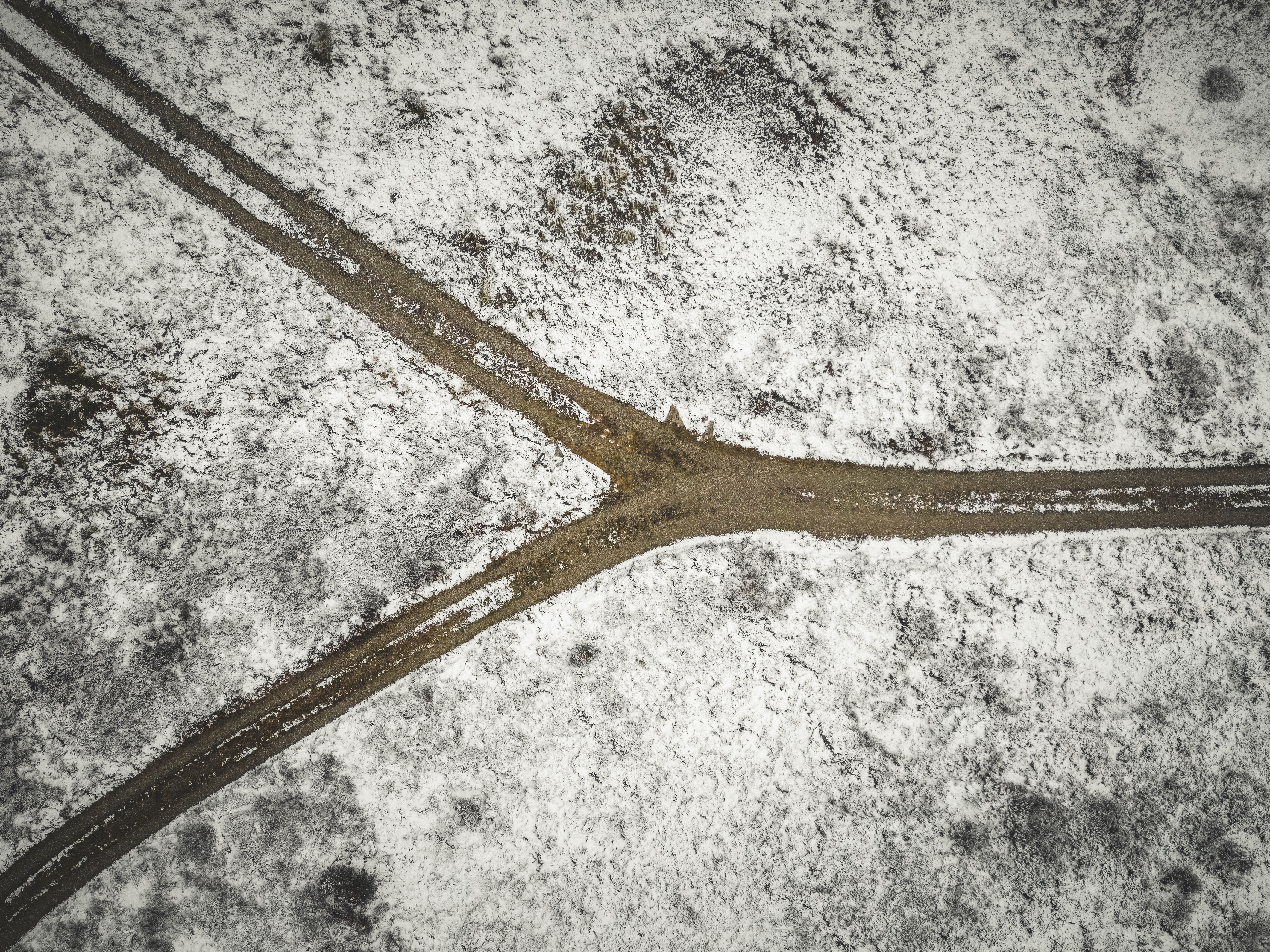 Drone shot of a snowy landscape with a forked dirt road in Bindslev, Denmark.