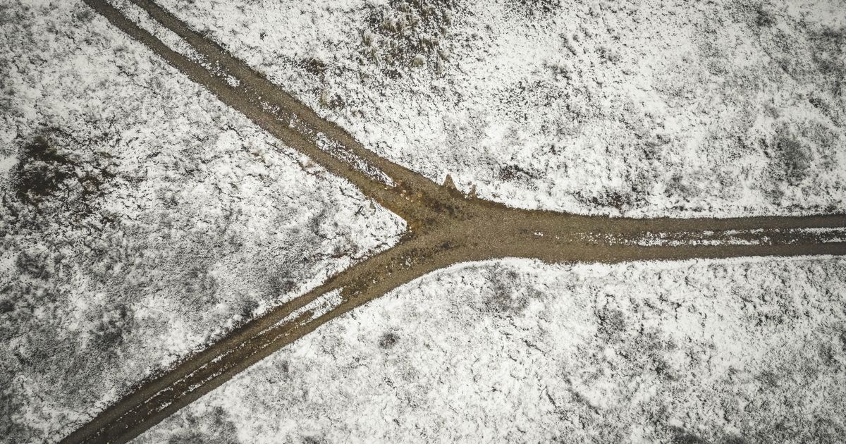 Drone shot of a snowy landscape with a forked dirt road in Bindslev, Denmark.