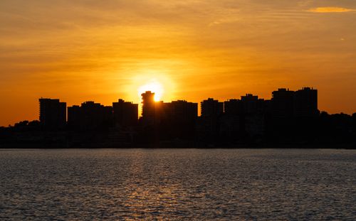 Free Stunning silhouette of a city skyline against a vibrant sunset over the water in Dehesa de Campoamor, Spain. Stock Photo