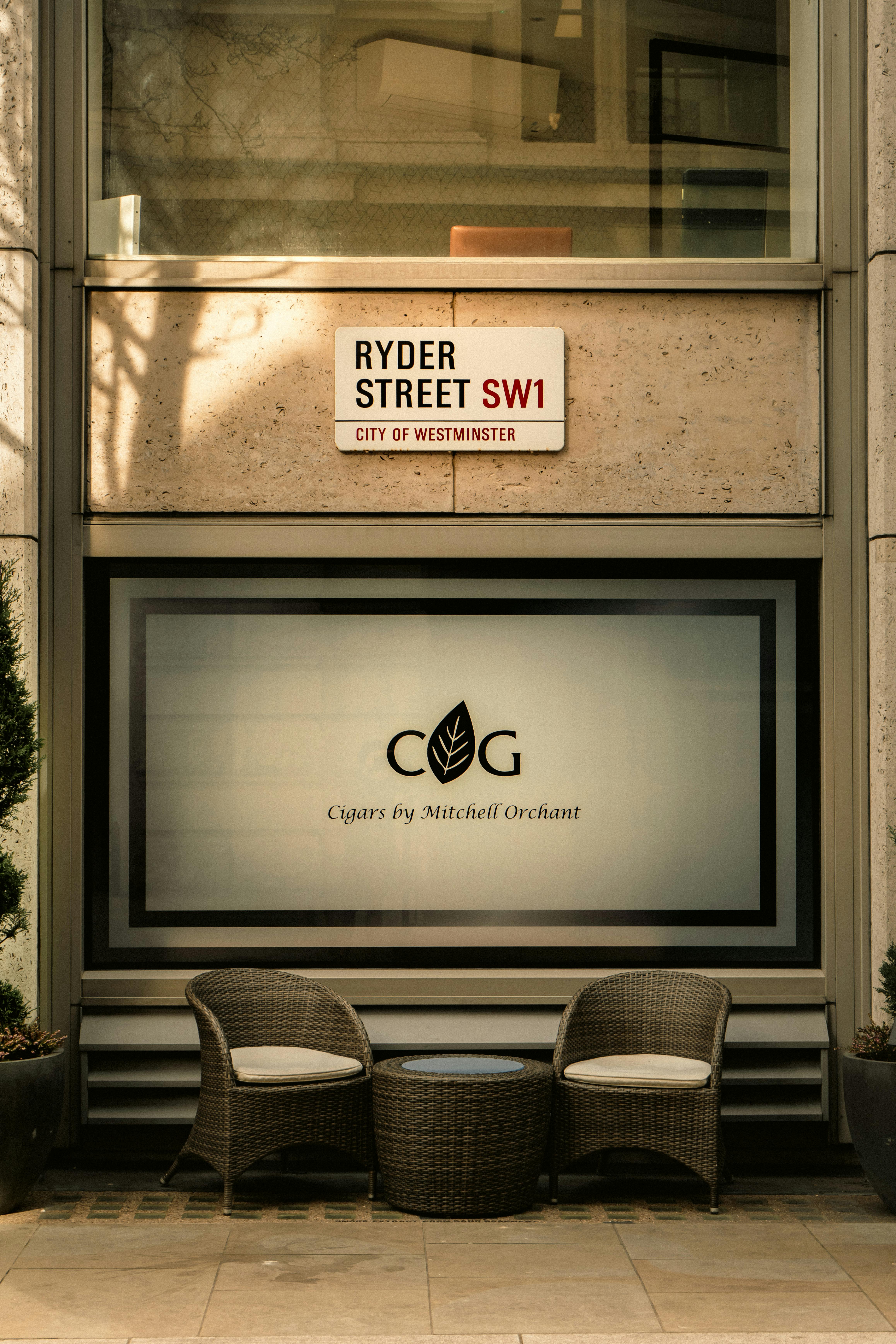 Cozy urban setting on Ryder Street in London, featuring wicker chairs and a cigar shop window.