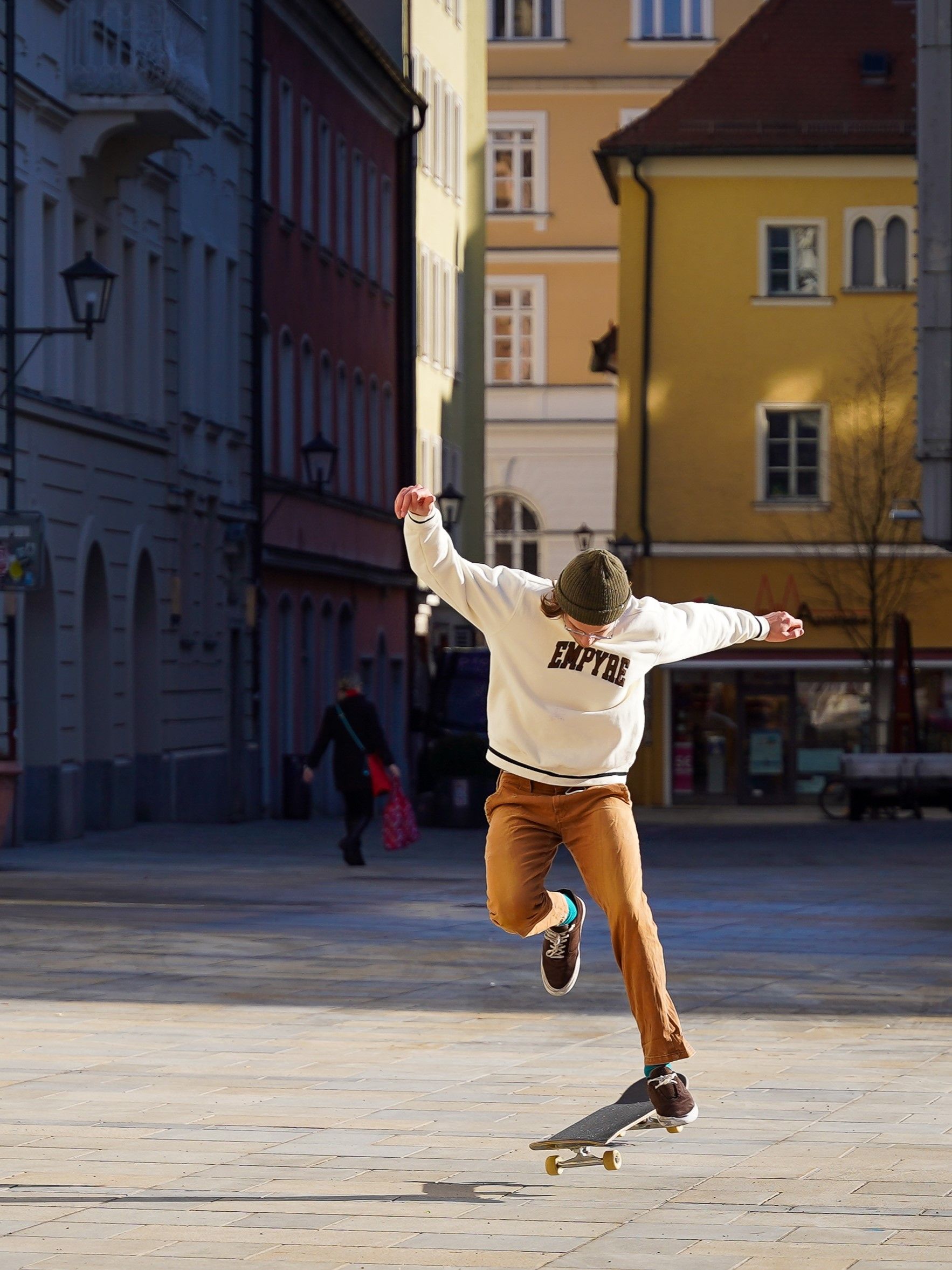 Young man skateboarding mid-air in a sunlit urban street.