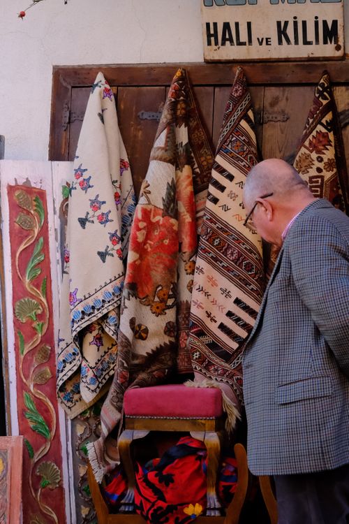 Free A man admires traditional Turkish rugs hanging in an urban setting, showcasing vibrant patterns. Stock Photo