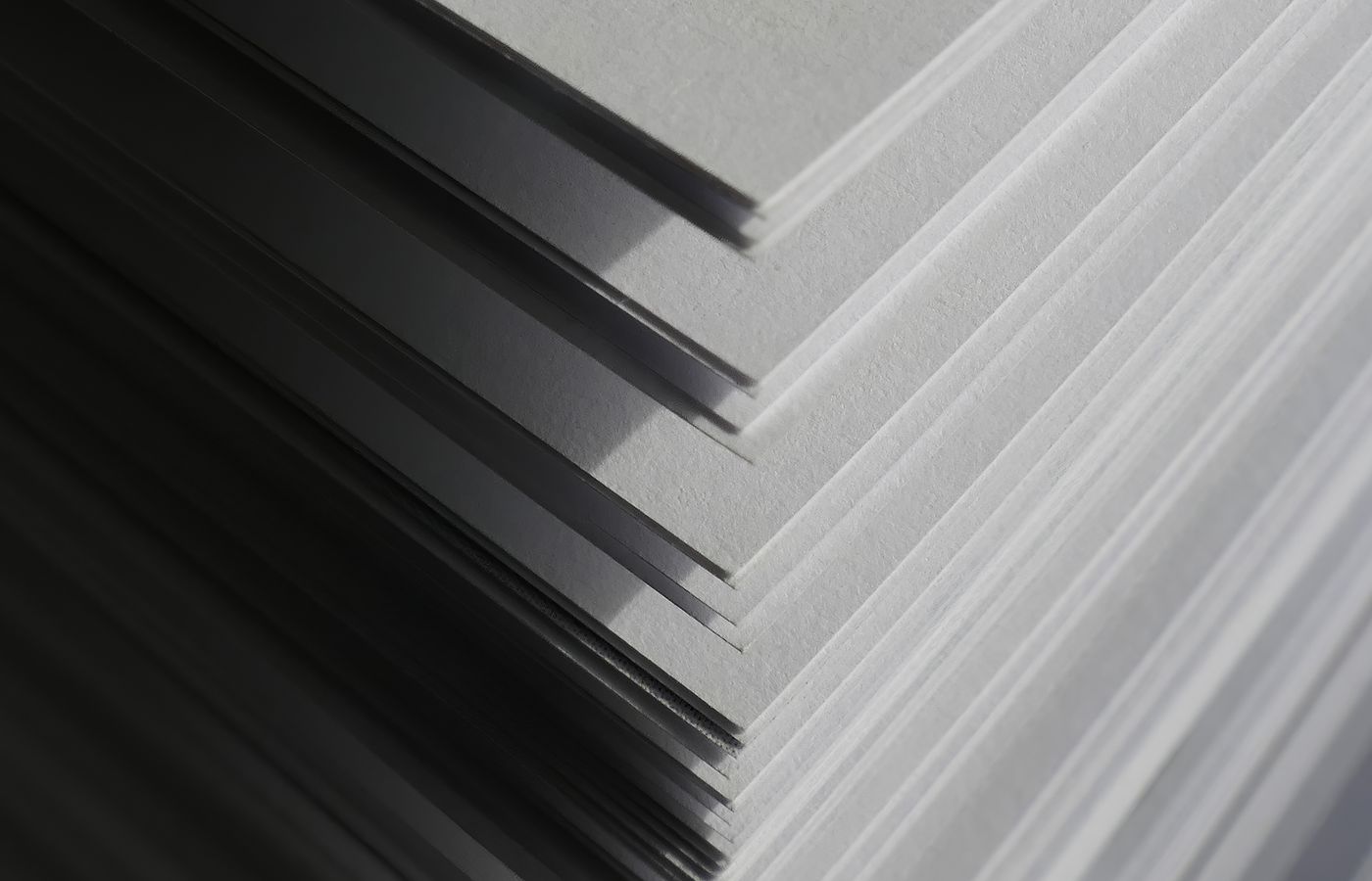 Artistic close-up of stacked white paper sheets creating geometric shadows and patterns in soft light.